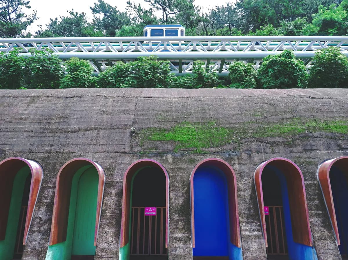 a row of blue, green, and red toilets next to a bridge
